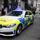 A BMW sedan police car passes crowd.